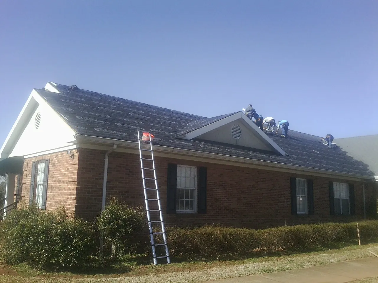 Crew tearing shingles off a brick ranch roof with a ladder set — Emergency Roof Repair work by our crew in Leoma