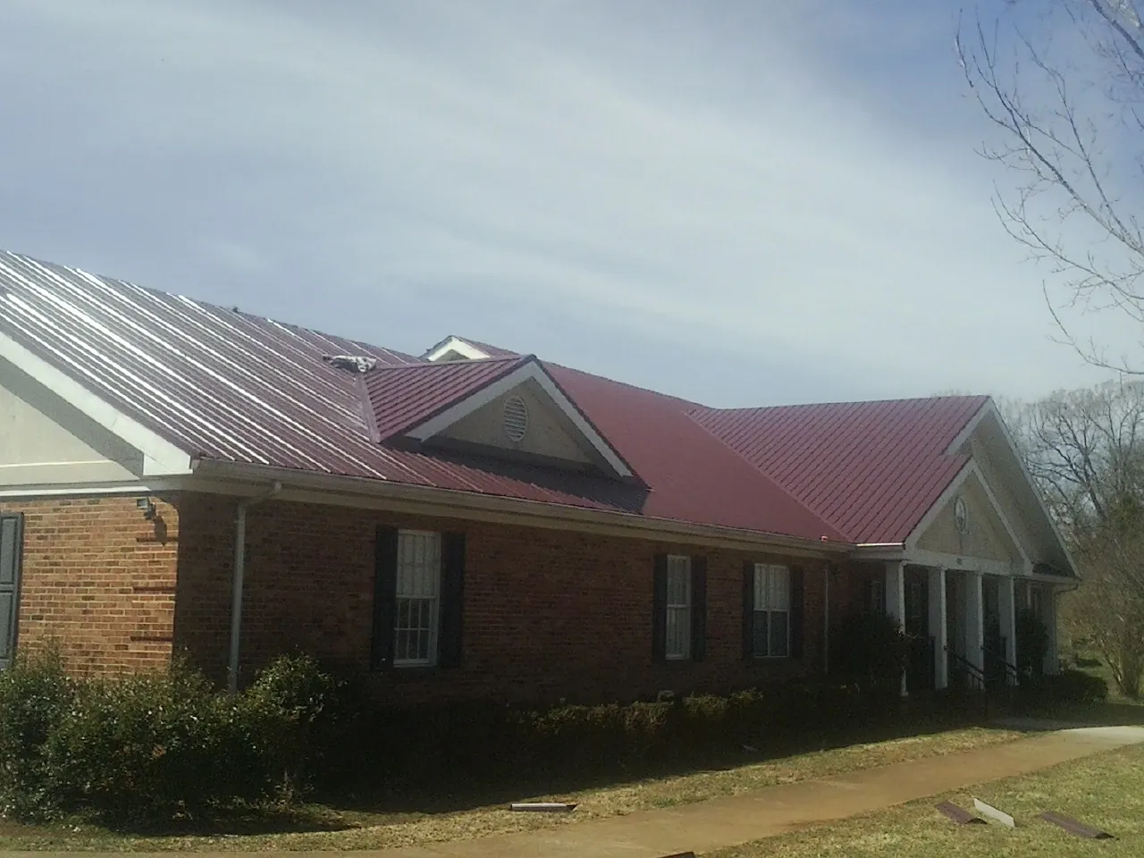 Red metal roof with gabled entries on a long brick building, from a Hail Damage Roof Repair job in Leoma