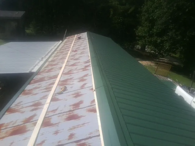 Old rusted panels beside newly installed green metal roofing — Wind Damage Roof Repair by Roofing Brothers in Leoma