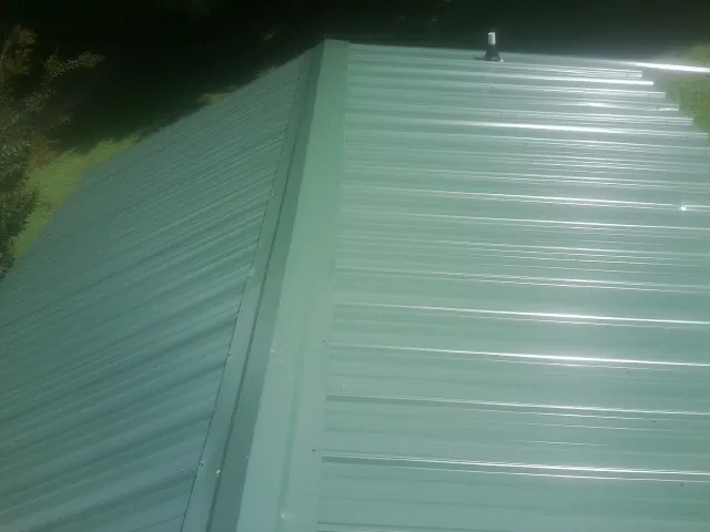 New green metal panels meeting at the ridge of a roof — Flat Roof Repair work by our crew in Leoma