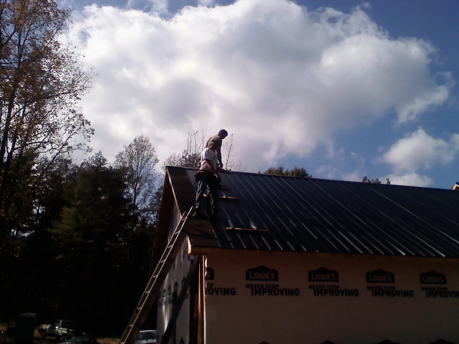 Roofer fastening dark metal panels high against a cloudy sky, from a Roof Inspection job in Leoma