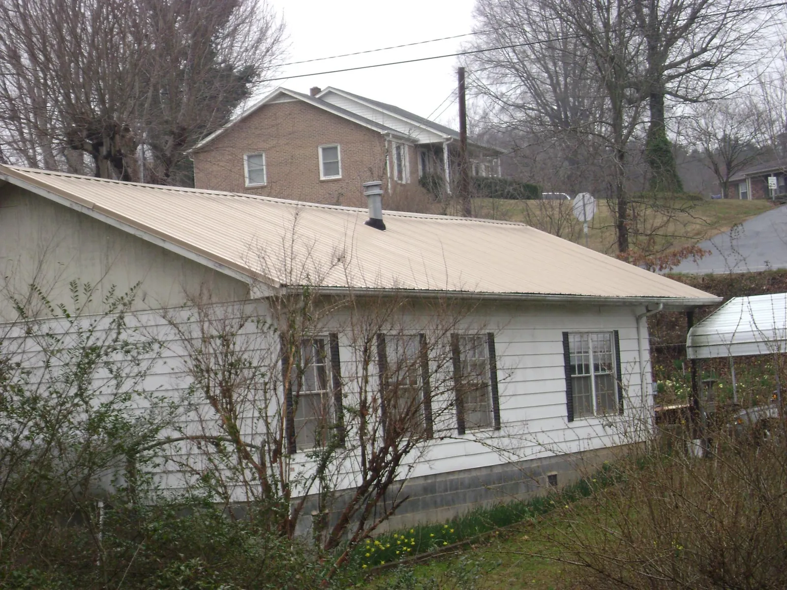 Tan metal roof on a white sided house set into a hillside — Commercial Roofing by Roofing Brothers in Leoma