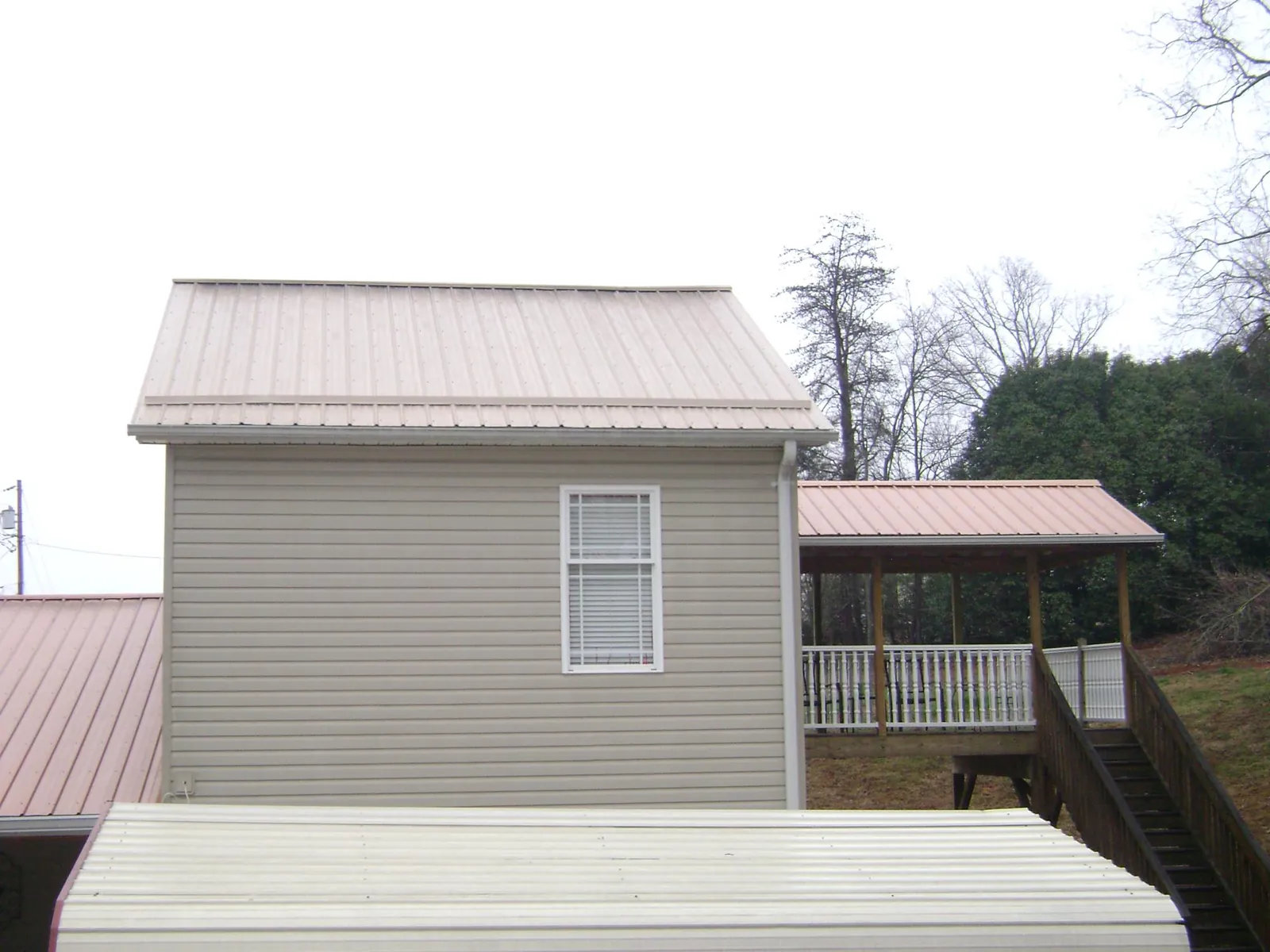 Tan metal roofs on a two story addition and attached porch, from a Roof Replacement job in Leoma